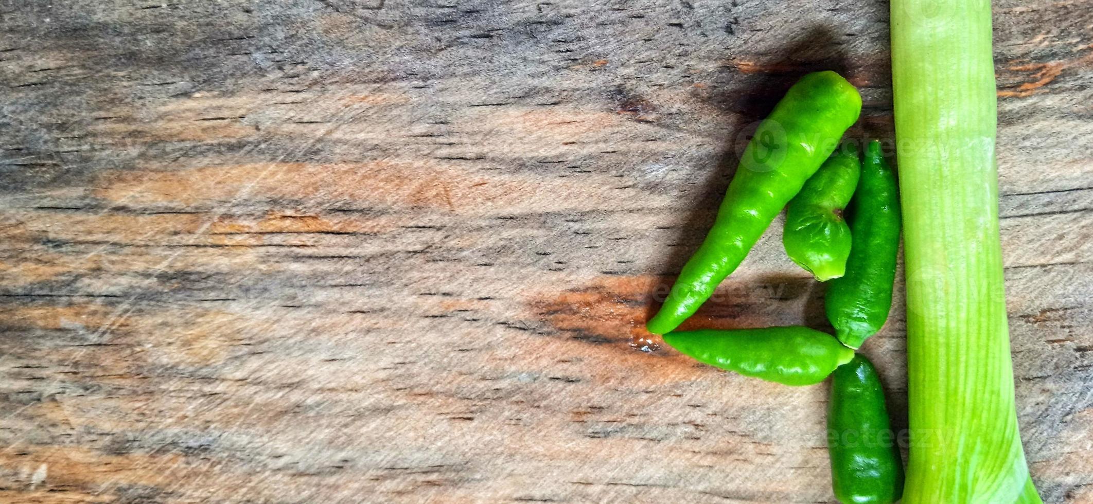 Vegetables of leek, garlic, and green chilli on the wooden cutting board. Vegetables ingredient background design. Suitable for advertising of food, drink, poster, backdrop, food company and industry. photo
