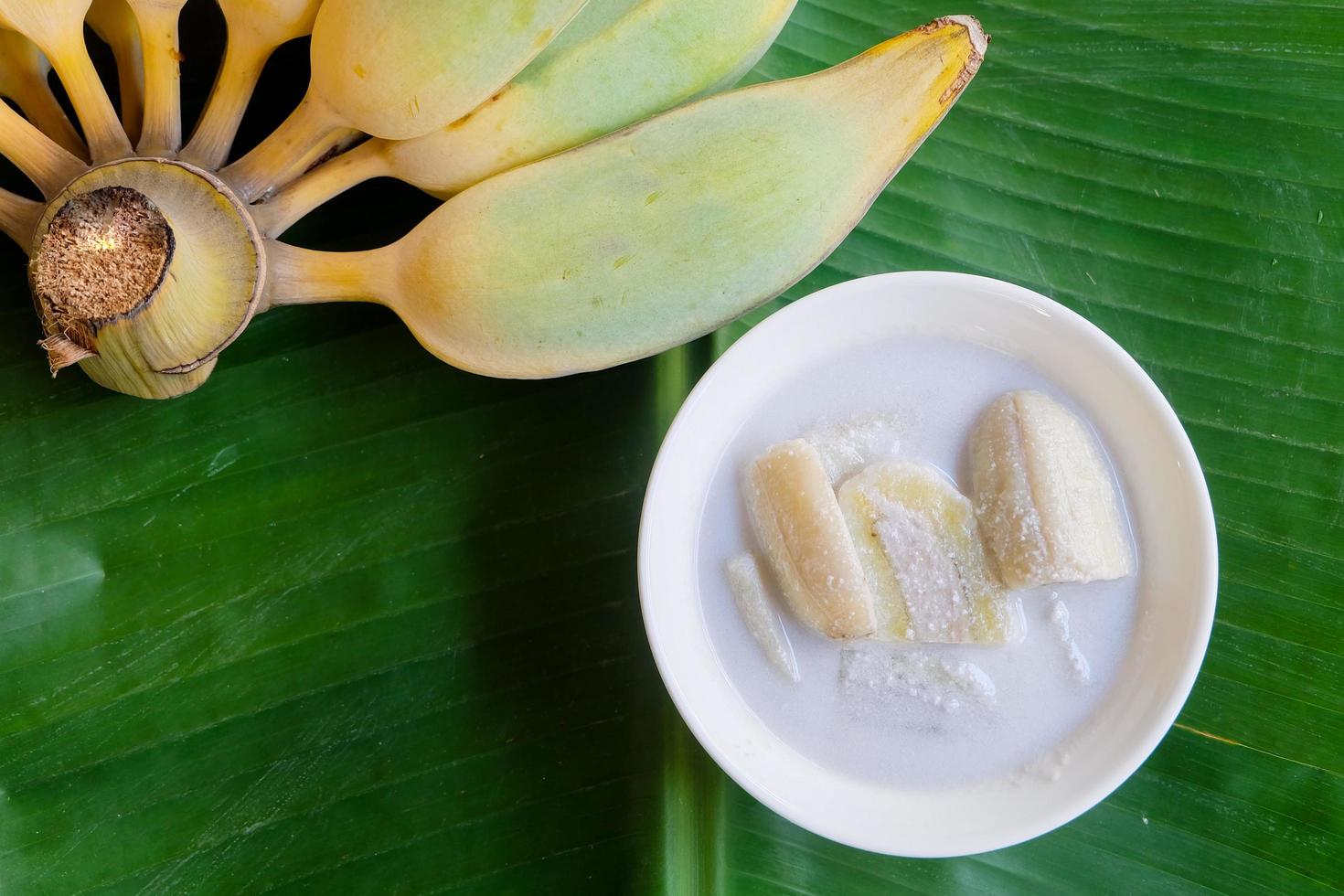 Close up and top view of Banana in coconut milk Thai popular dessert. in white bowl  on green banana leaf background. photo