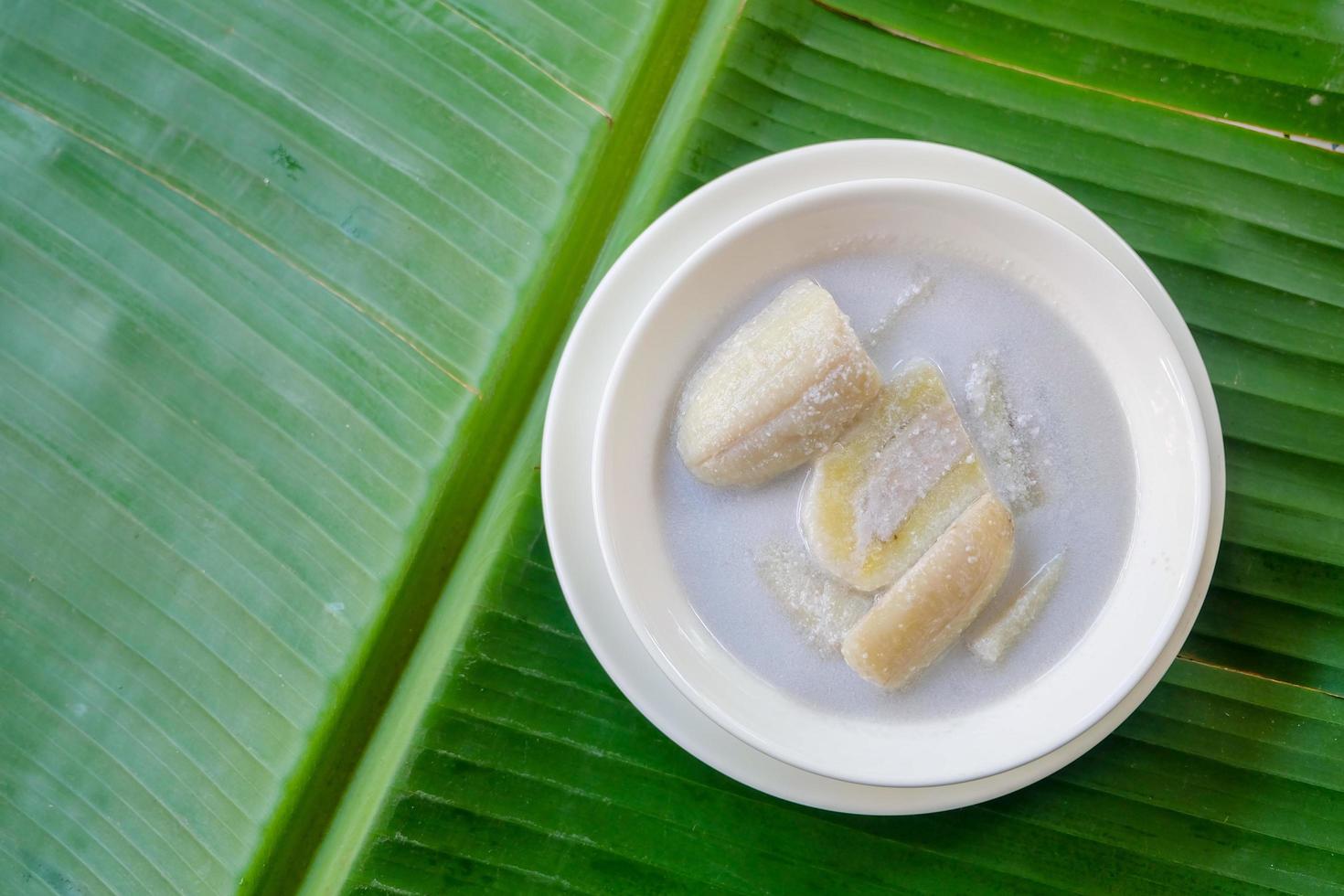 Close up and top view of Banana in coconut milk .Thai popular dessert. in white bowl on green banana leaf background. photo