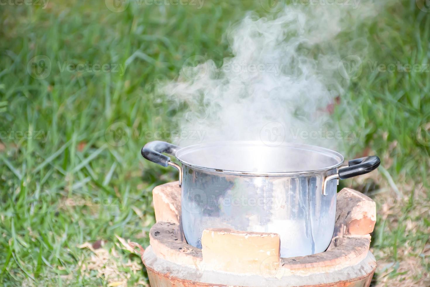 Boil soup in a stainless steel pot. Dinner is hot on the charcoal grill. White smoke from the heat. Grass blurred background. Closeup and selective focus. photo