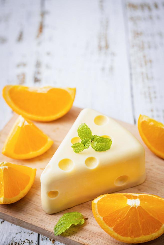 Homemade of Fresh white chocolate cake in a slice of cheese shape putt on white wooden table and mint, orange. Sweet Food and Dessert concept. Sweets decorated for holiday. Close-up dessert view. photo