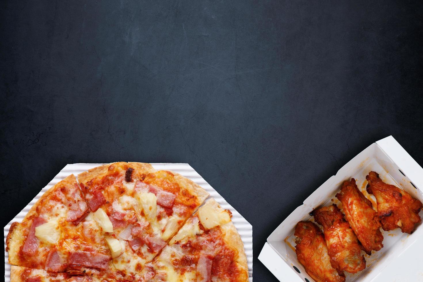 Food delivery box set. Hawaiian Thin Crust Pizza on a paper tray, Grilled Chicken BBQ on wooden, placed on a gray-black concrete with copy space. Top view. photo