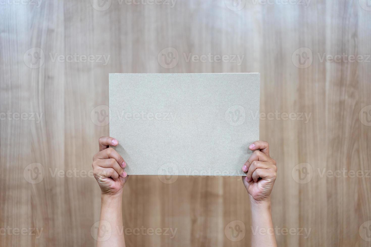 Asian person is holding and raising up the empty a4 paper on the wood background. photo
