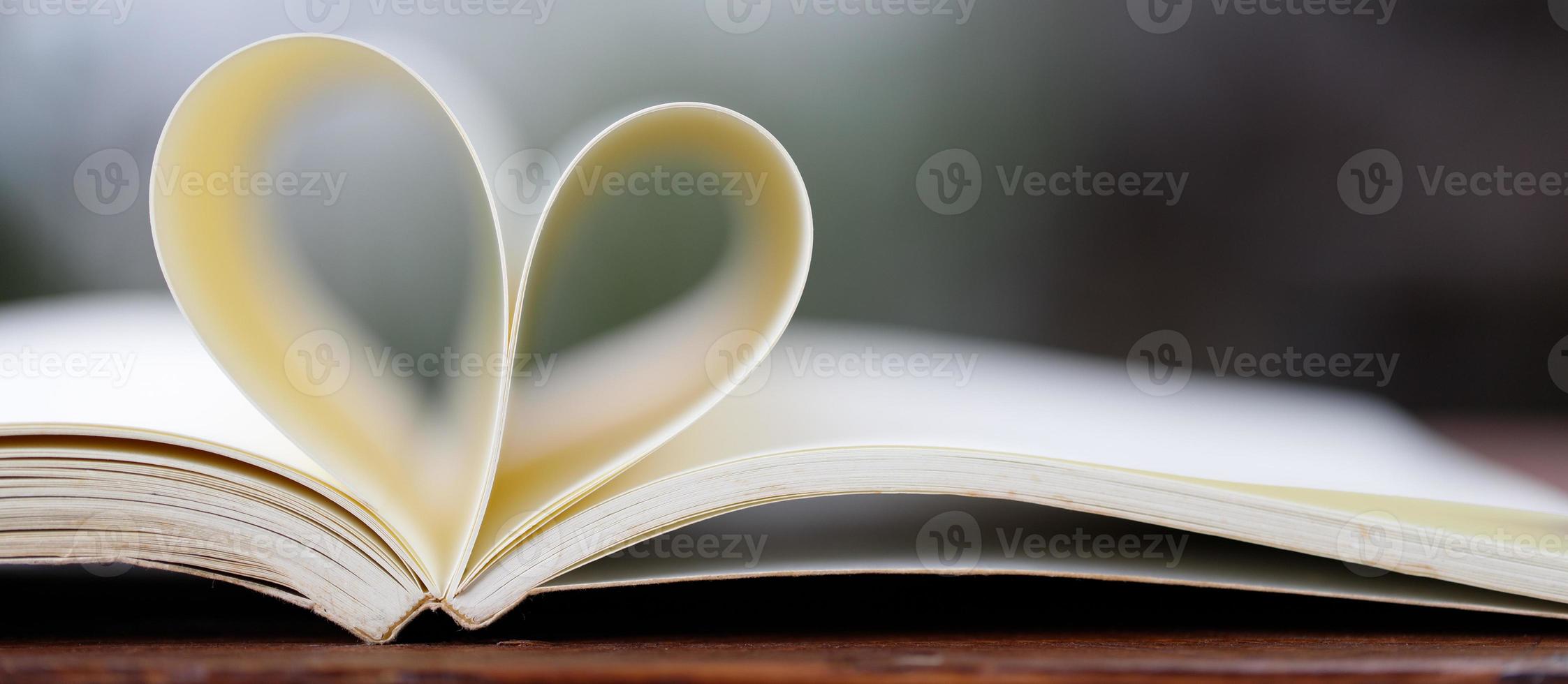 Close up heart shape from paper book on wooden table with vintage blur background photo