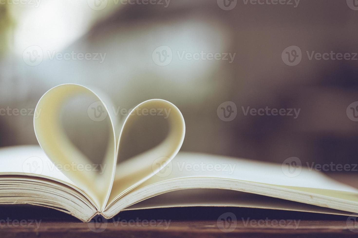 Close up heart shape from paper book on wooden table with vintage blur background photo