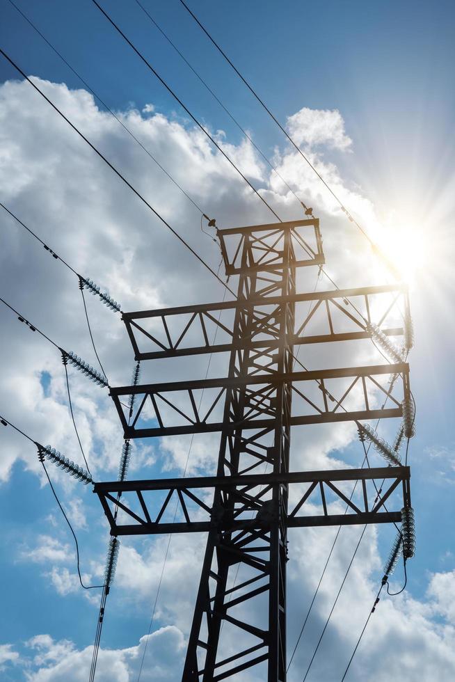 torre de esquina de transmisión eléctrica de alto voltaje contra el fondo de un cielo nublado con rayos de sol. foto