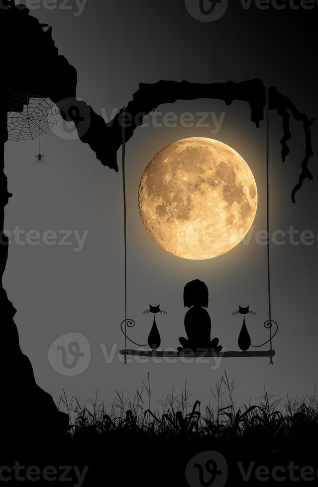 Halloween night background with moon, spider and the girl and the two cats sitting on swings under the old tree. photo