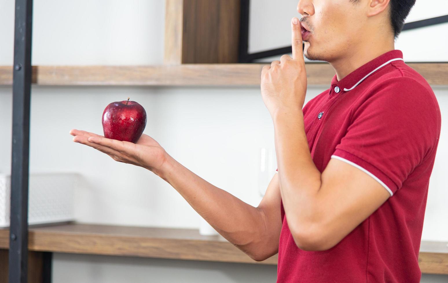 Healthy lifestyle and freshness concept. Smart, young and healthy Asian man eating apple in the loft style kitchen room. photo