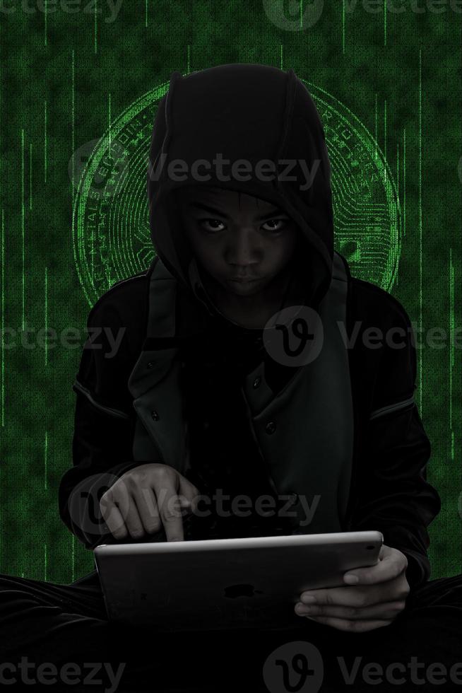 Hacker boy are hacking through the tablet on green symbols background. photo
