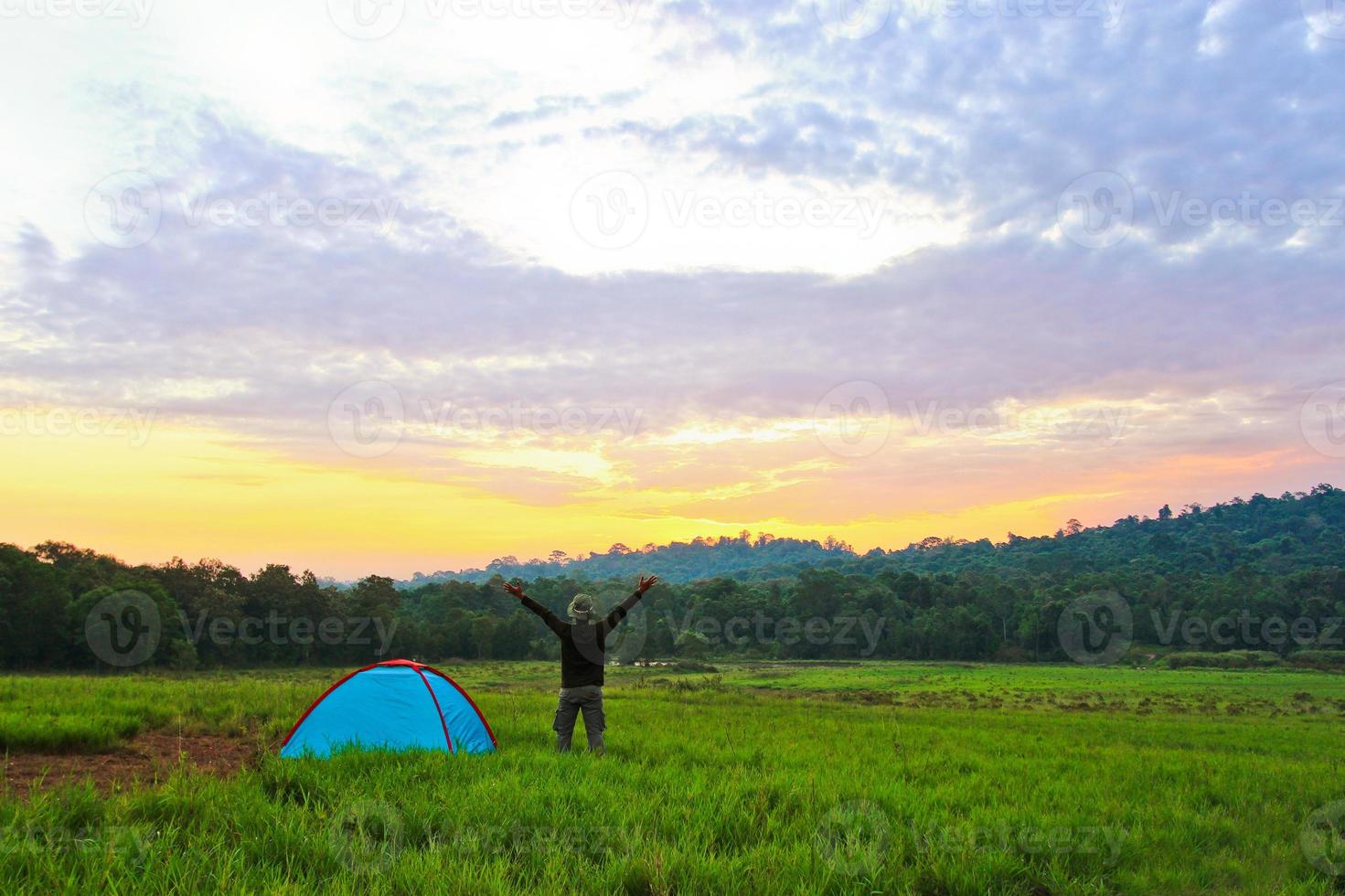 The man who stand next to the tent in the meadow put his hand up  with wide sky and cloud photo