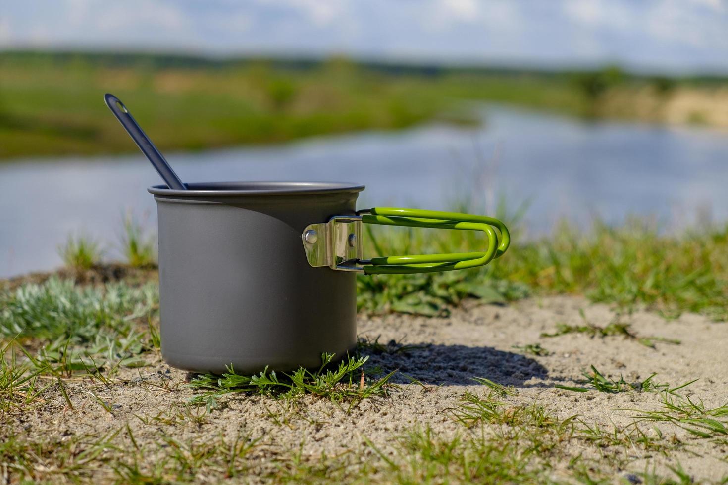 Camping pot and spoon on river background photo