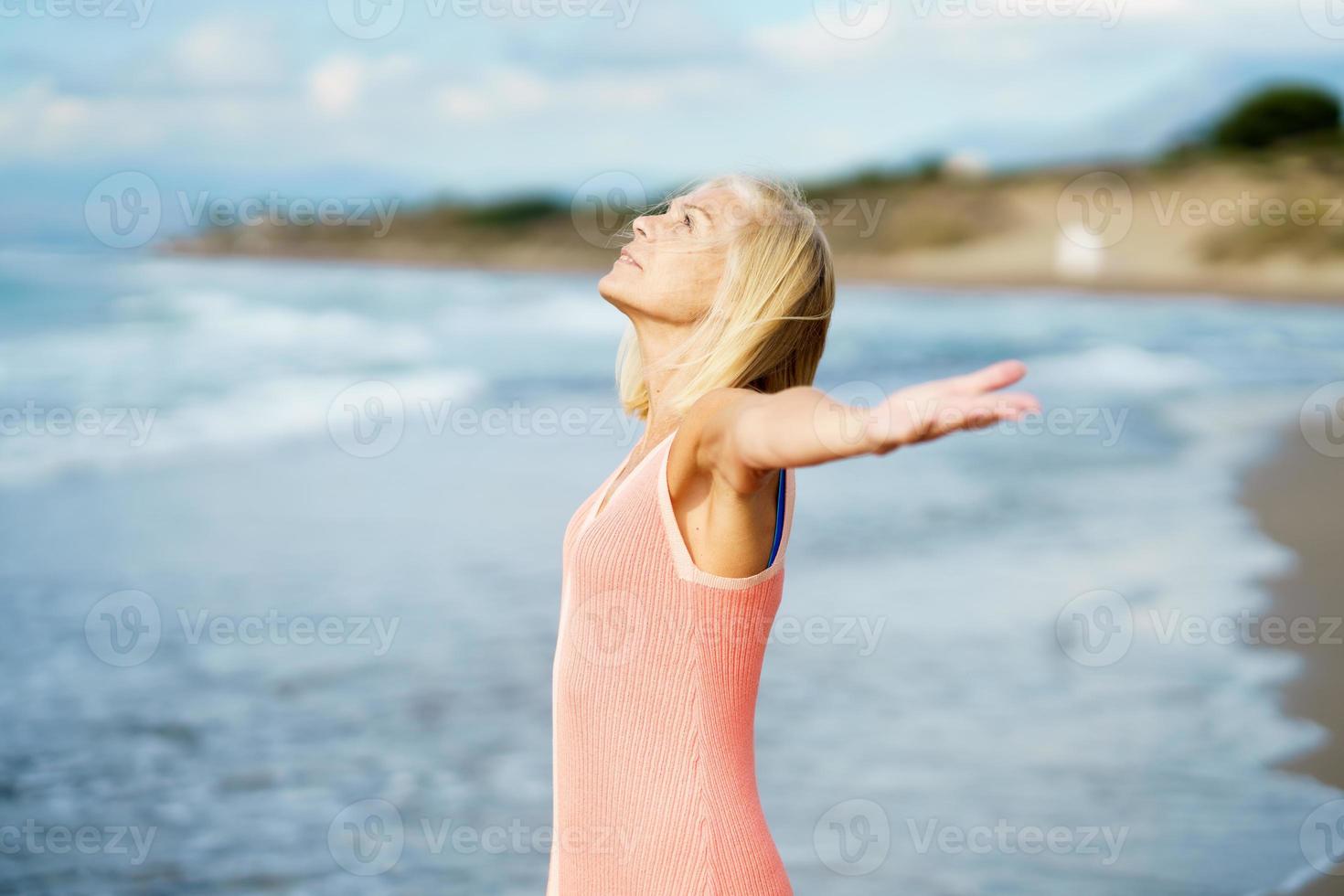 Beautiful mature woman opening her arms on a beautiful beach, enjoying her free time photo