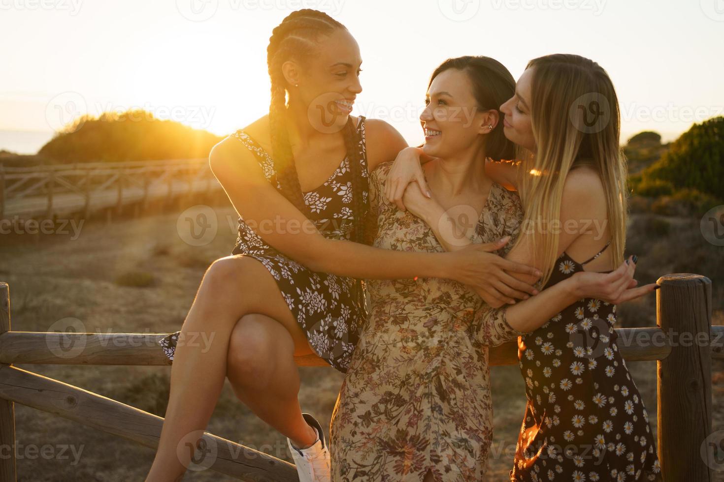 Happy diverse girlfriends hugging near fence photo