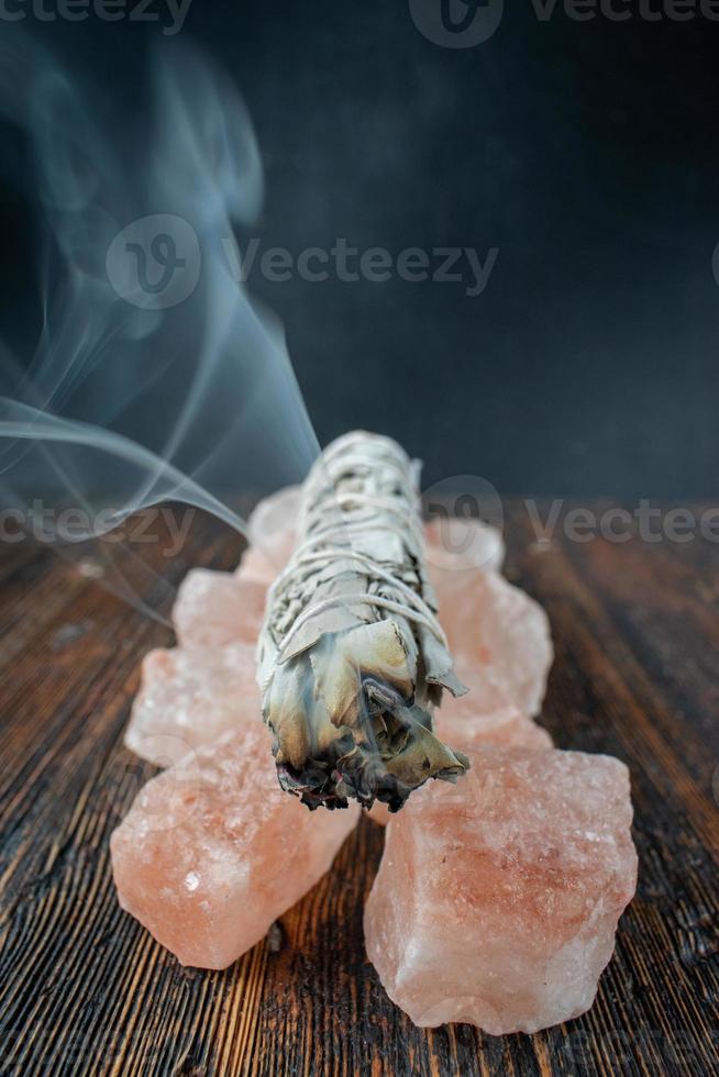 burning a smudge sage stick on a base of pink salt crystals with smoke trail photo