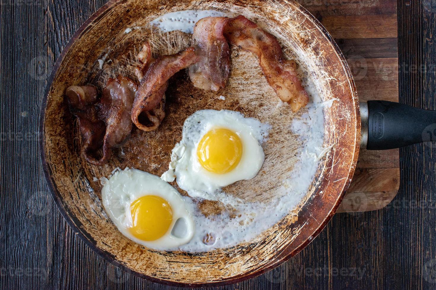 homemade breakfast of bacon and sunny side-up eggs in frying pan flat lay photo