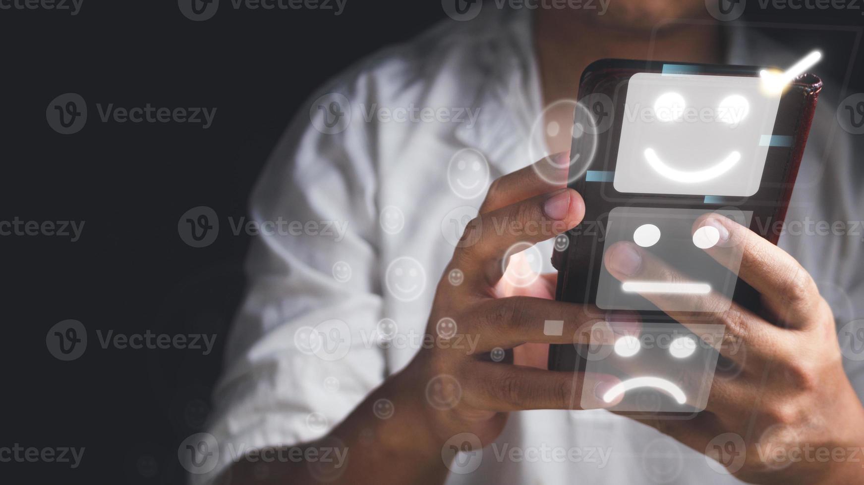 concepto de evaluación y satisfacción. el hombre elige una emoción de sonrisa que es una excelente revisión con un modelo de teléfono móvil no identificado. primer plano medio sobre fondo negro. foto