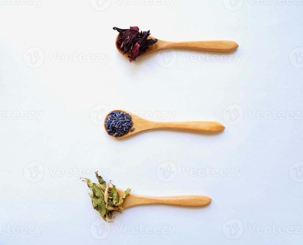 Top view of three wooden spoons with dried tea leaves of lime, hibiscus, lavender, eco-friendly minimalist concept photo