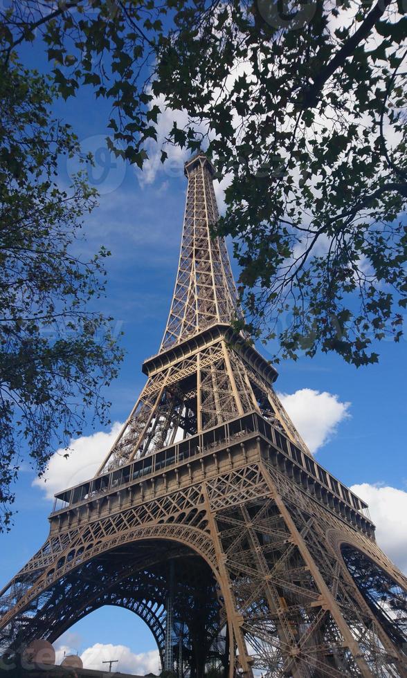 The most beautiful symbol of Paris, the Eiffel tower low angle view, with trees and leaves on the foreground photo