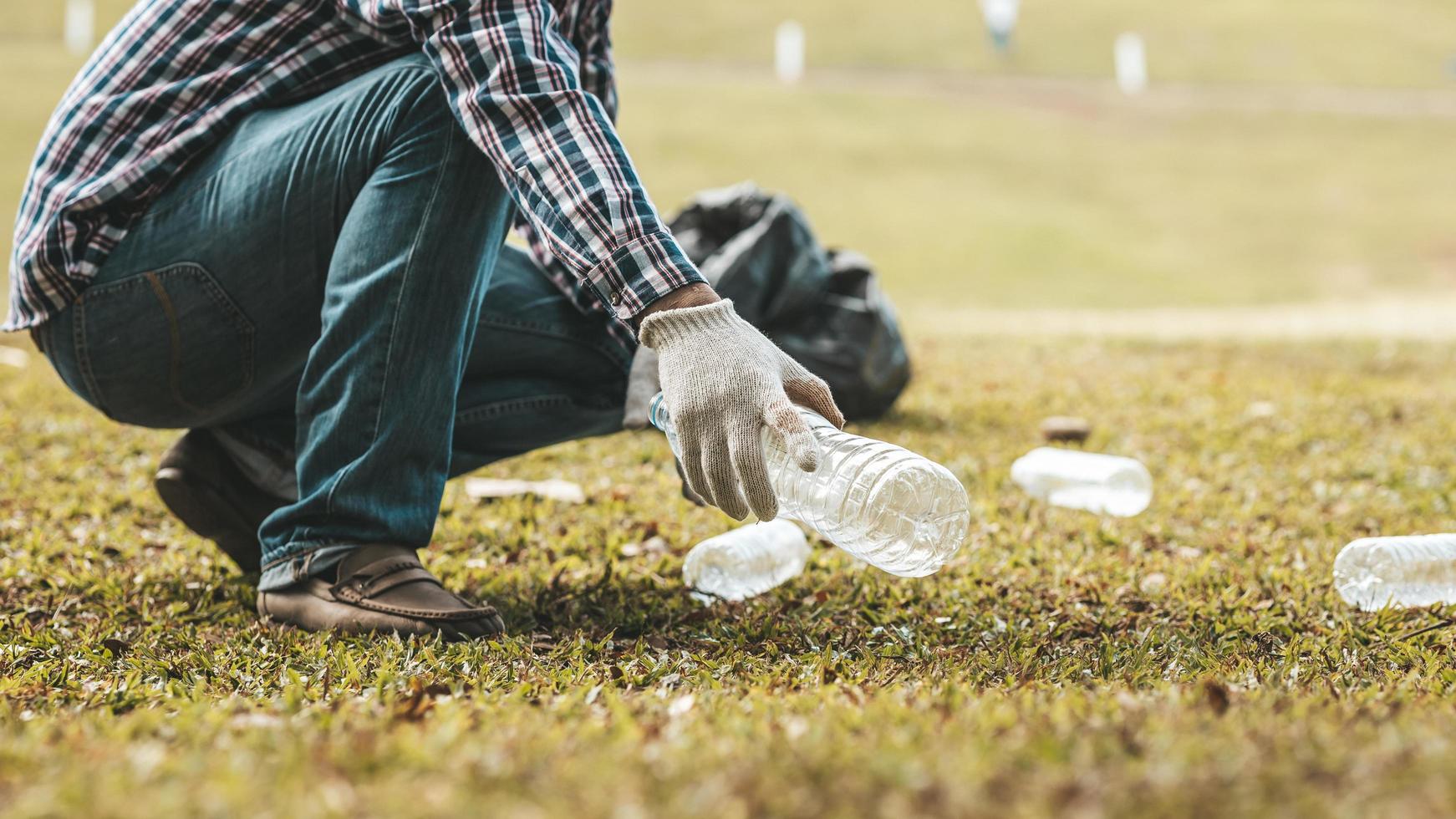 A man is picking up trash in a park, not throwing trash in the trash can ruin the beauty of the garden area and also cause global warming and harm animals. Concept of cleanliness in public areas. photo