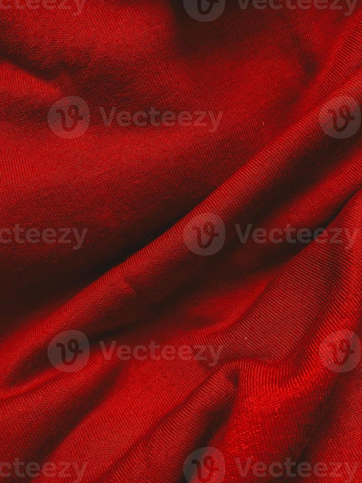 Red fabric cloth texture background with wavy folds and shadows, closeup, vertical photo. Abstract textile material, elegant wallpaper design, top view photo