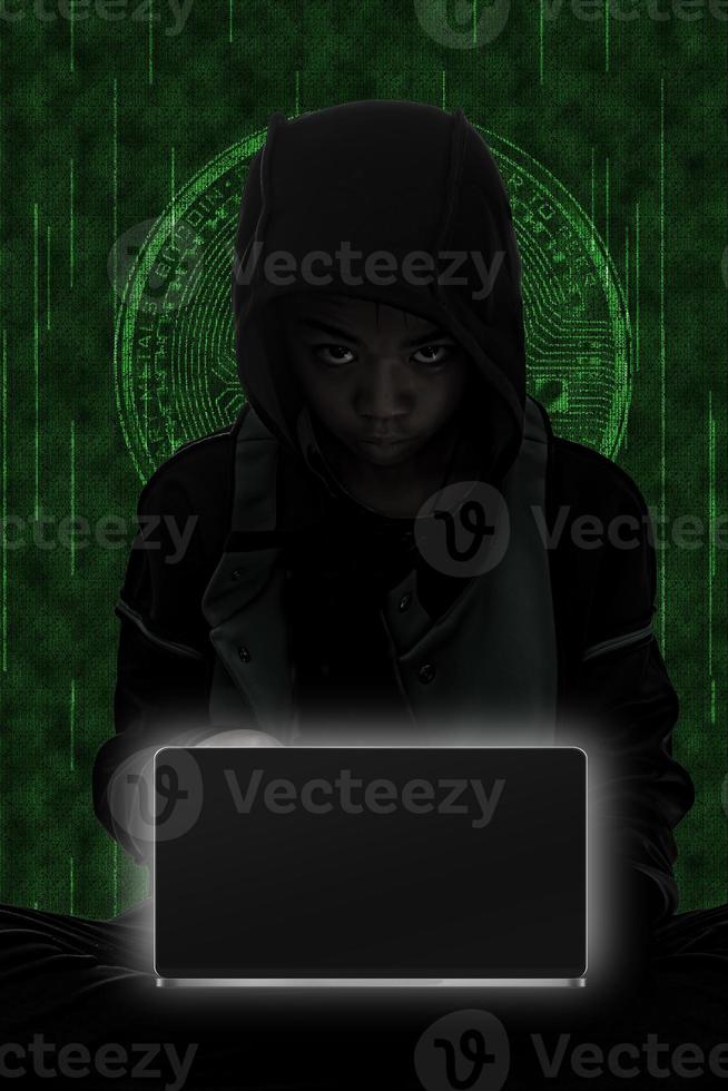 Hacker boy are hacking through the laptop on green symbols background. photo