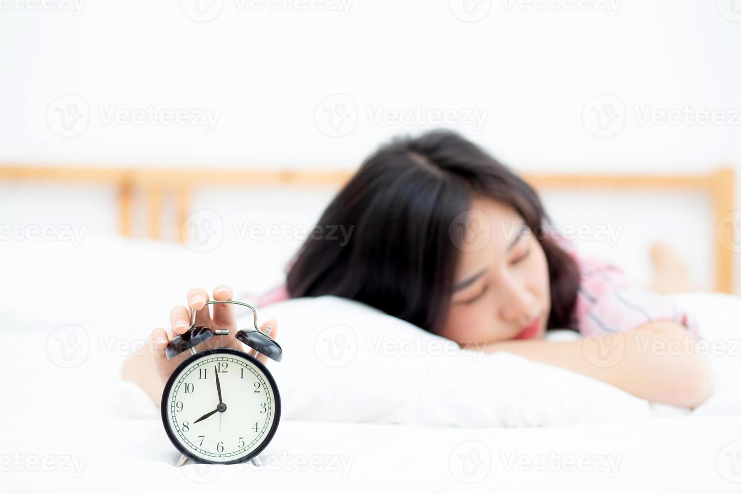 Beautiful asian young woman turn off alarm clock in morning, wake up for sleep with alarm clock, relax and lifestyle concept. photo