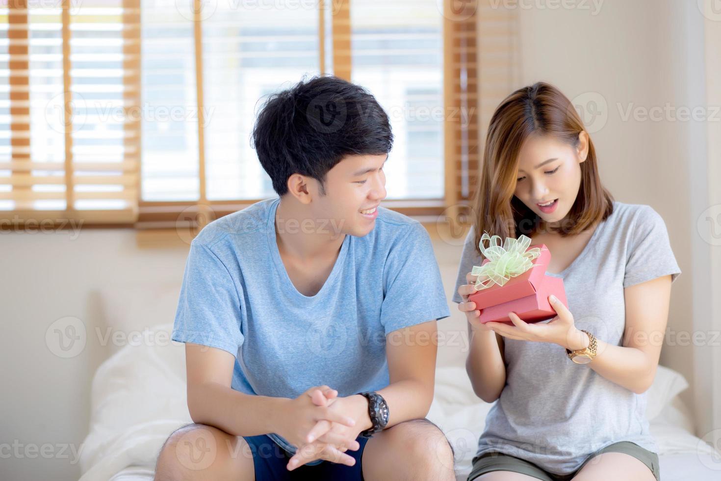 hermosa joven pareja asiática enamorada caja de regalo sorpresa en el dormitorio en casa, aniversario familiar con disfrute y romántico juntos esposa y esposo con relación, celebrando el concepto de día de san valentín. foto