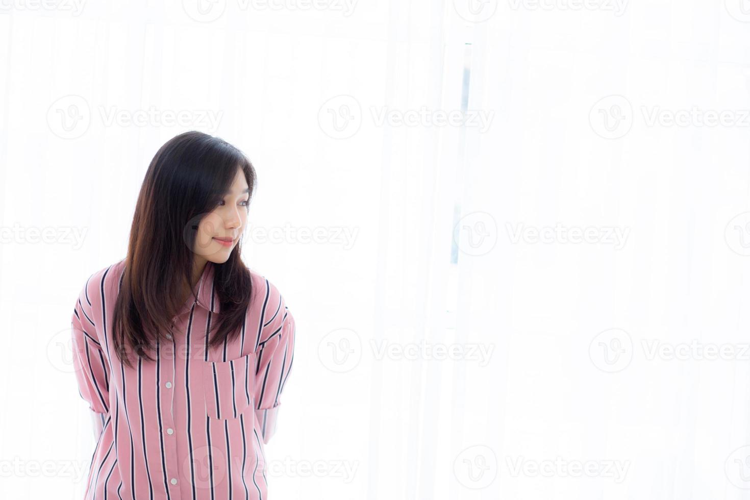 Portrait of beautiful young asian woman standing the window and smile while wake up with sunrise at morning, lifestyle and relax concept. photo