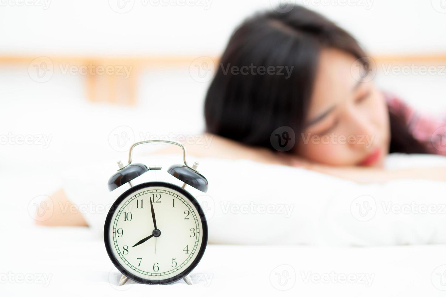 closeup alarm clock and beautiful asian young woman in morning, wake up for sleep with alarm clock, relax and lifestyle concept. photo