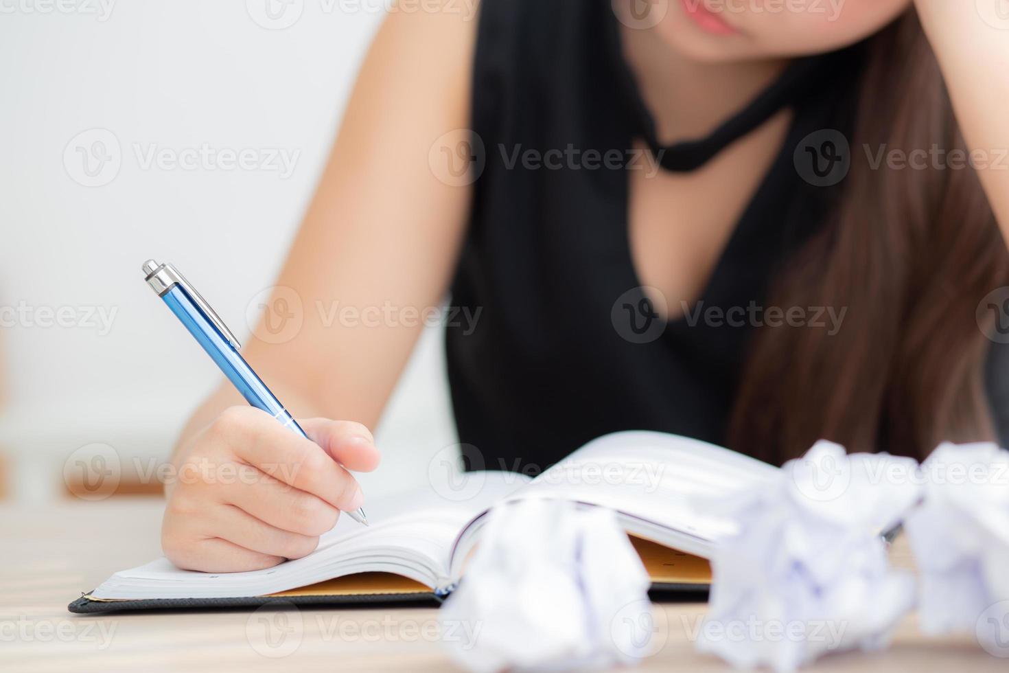 hermosa mujer asiática cansada y estresada por escribir con exceso de trabajo en el escritorio, chica preocupada sin idea con cuaderno y papel arrugado en la oficina, concepto independiente y de negocios. foto