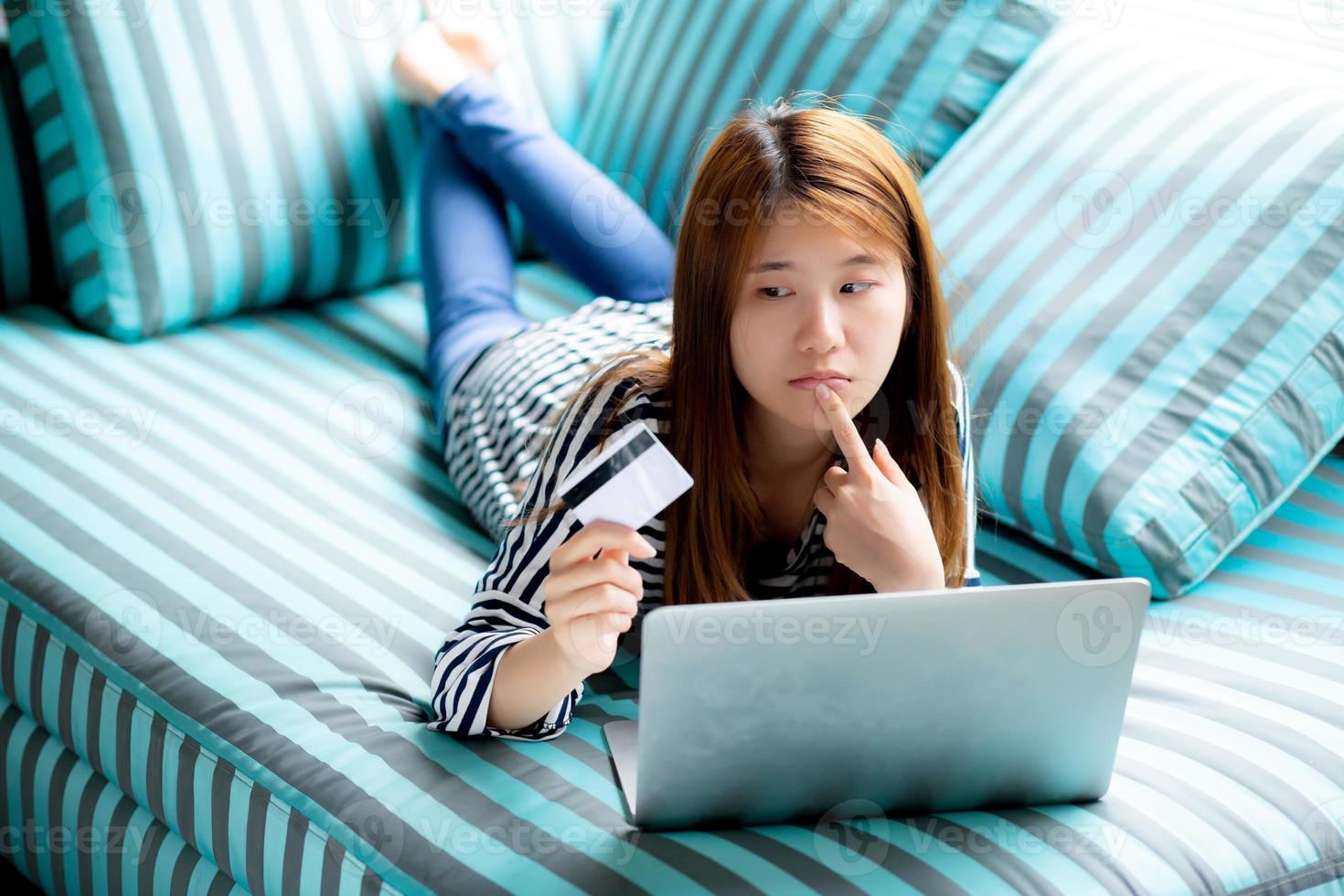 Beautiful of portrait young asian woman lying think use credit card with laptop, Content girl shopping online and payment with notebook computer on sofa, lifestyle concept. photo