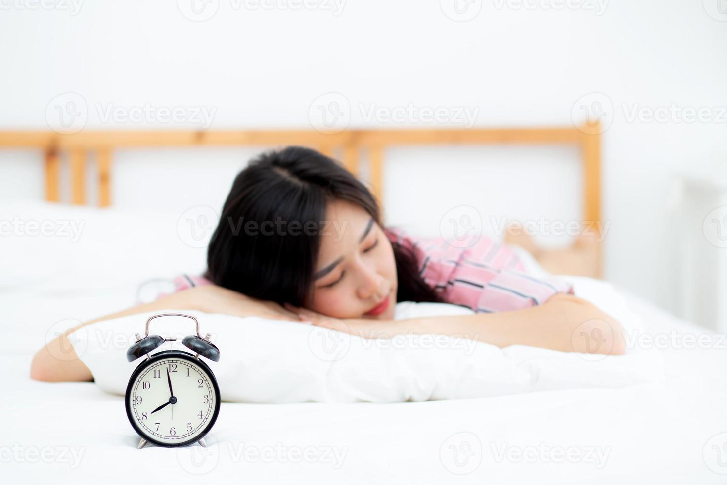 closeup alarm clock and beautiful asian young woman in morning, wake up for sleep with alarm clock, relax and lifestyle concept. photo