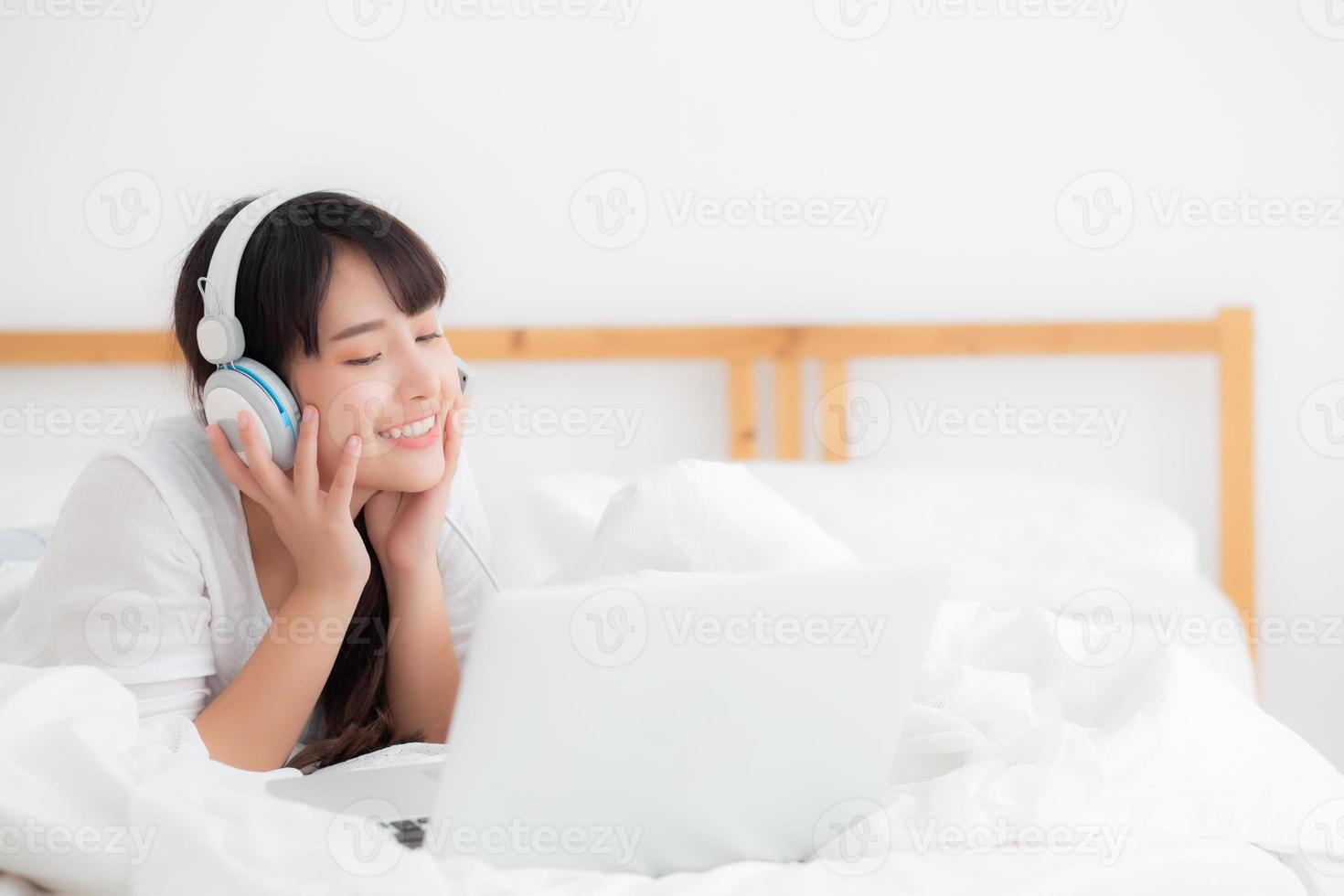 Beautiful young asia woman lying in bedroom using laptop computer showing video call chat at home, girl greet and listen and talking messenger, communication and lifestyle concept. photo