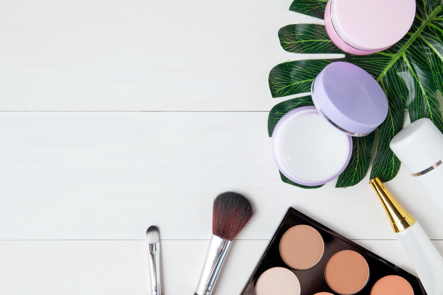 maquillaje cosmético y producto para el cuidado de la piel y hojas en una mesa de madera blanca, belleza con crema de tratamiento y espacio para copiar humectante en un escritorio de madera, concepto de salud y bienestar, vista superior. foto