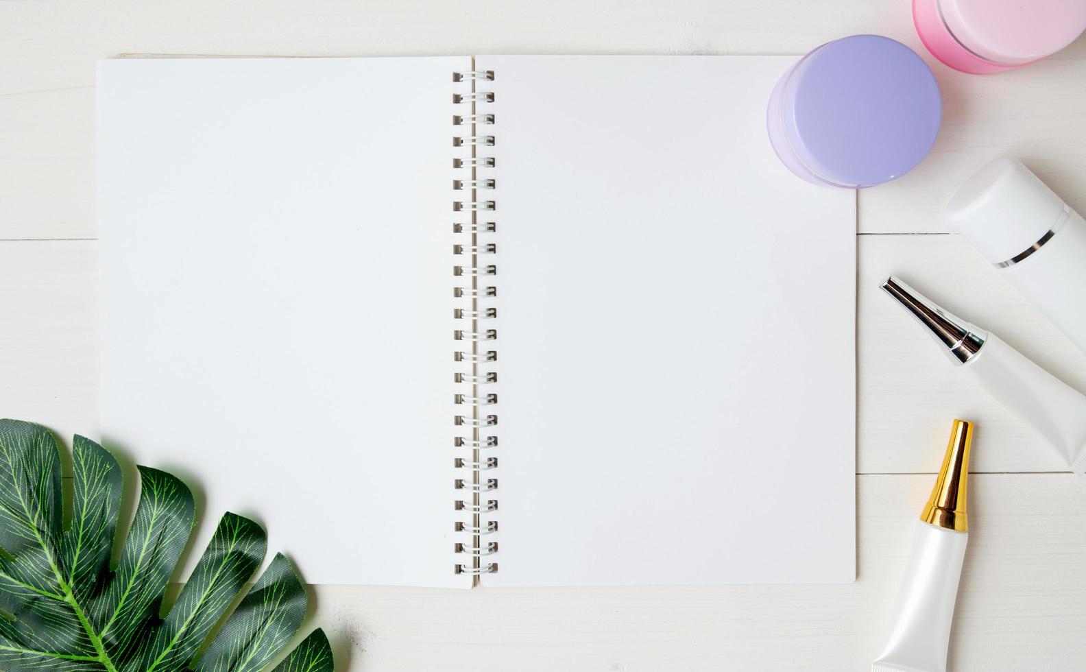 cosmetic and skin care product and notebook and leaves on table, beauty with treatment cream and moisturizing and notepad copy space on wooden desk, health and wellness concept, top view. photo
