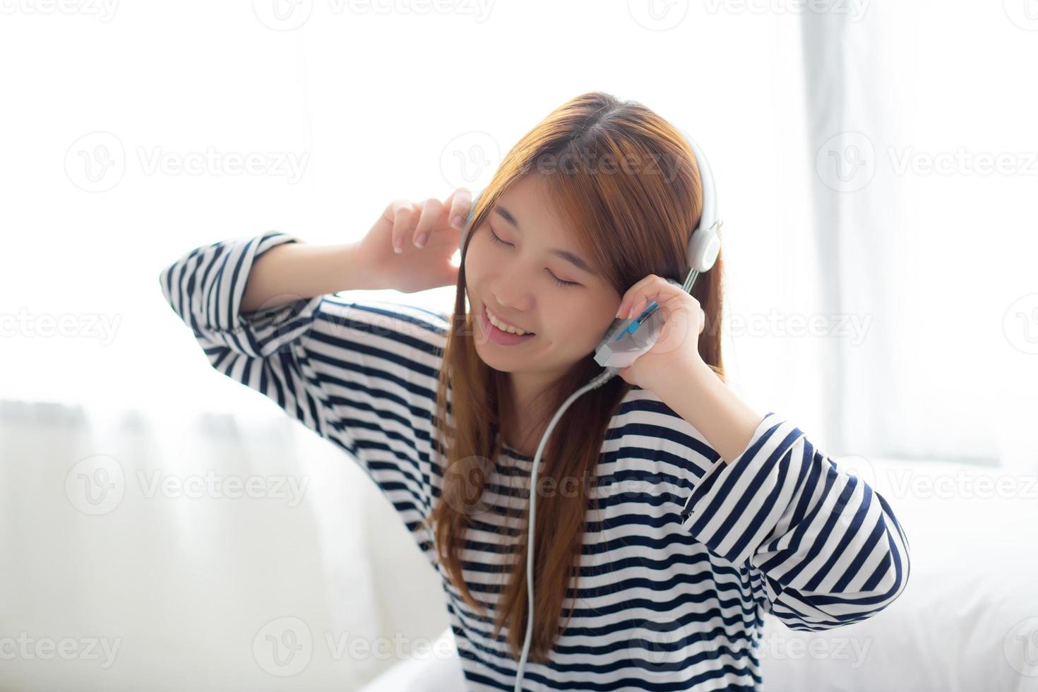 hermosa mujer joven asiática disfruta y se divierte escuchando música con auriculares sentados en el dormitorio, la chica se relaja con el concepto de auriculares, ocio y tecnología. foto