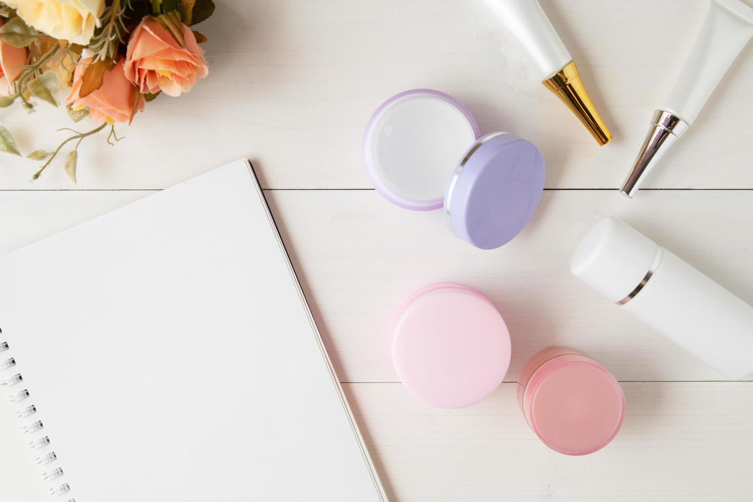 cosmetic and skin care product and notebook and leaves on table, beauty with treatment cream and moisturizer and notepad copy space on wooden desk, health and wellness concept, top view. photo