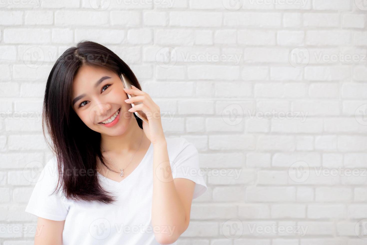hermosa de retrato joven mujer asiática habla teléfono inteligente y sonríe de pie sobre fondo de ladrillo de cemento, teléfono de llamada femenina independiente, comunicación de concepto móvil. foto
