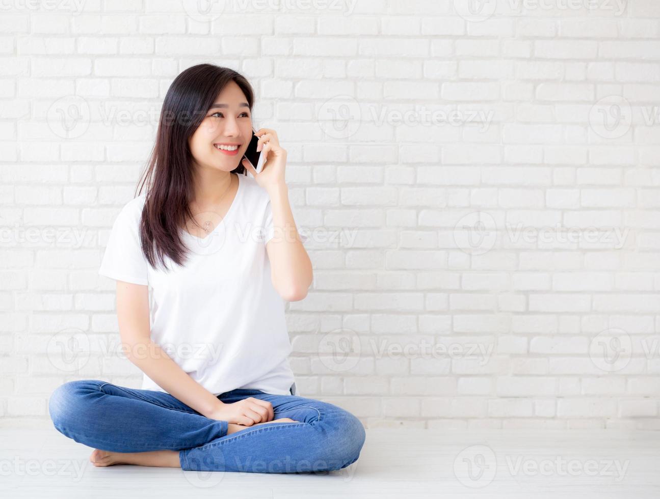 Beautiful of portrait young asian woman talk smart phone and smile sitting on cement concrete brick background, freelance female calling telephone, communication of mobile concept. photo