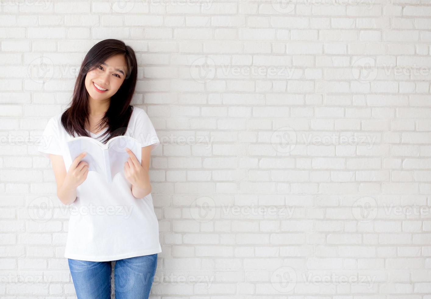 Beautiful of portrait young asian woman happiness relax standing reading book on concrete cement white background at home, girl happy study content literature, education and lifestyle concept. photo