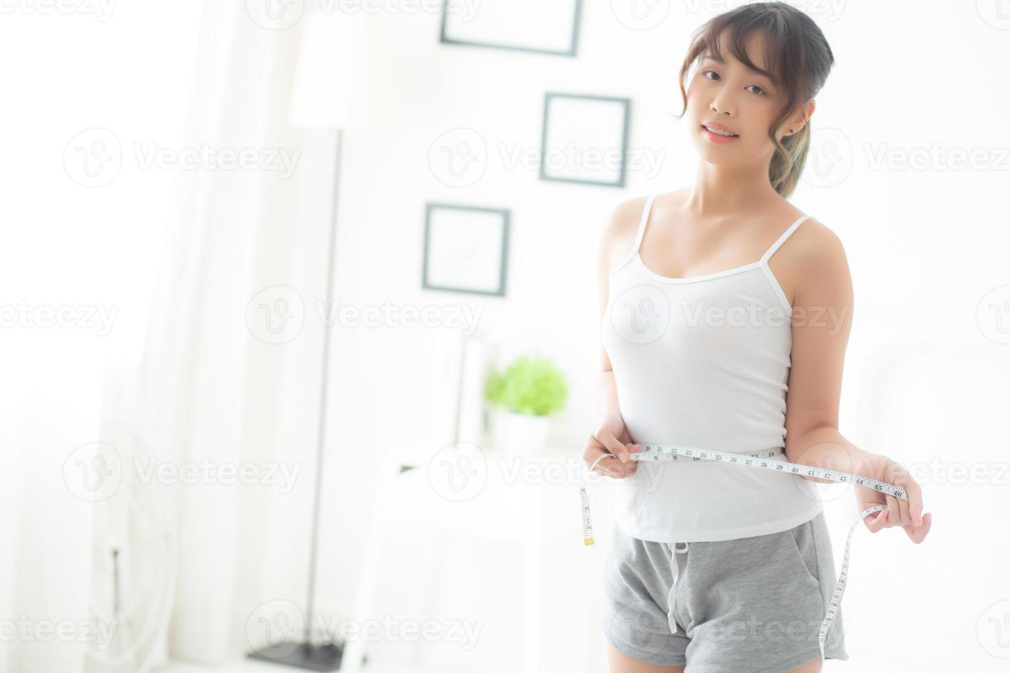 Beautiful young asian woman body diet and slim with measuring waist for weight in the bedroom, girl have cellulite and calories loss with tape measure, health and wellness concept. photo