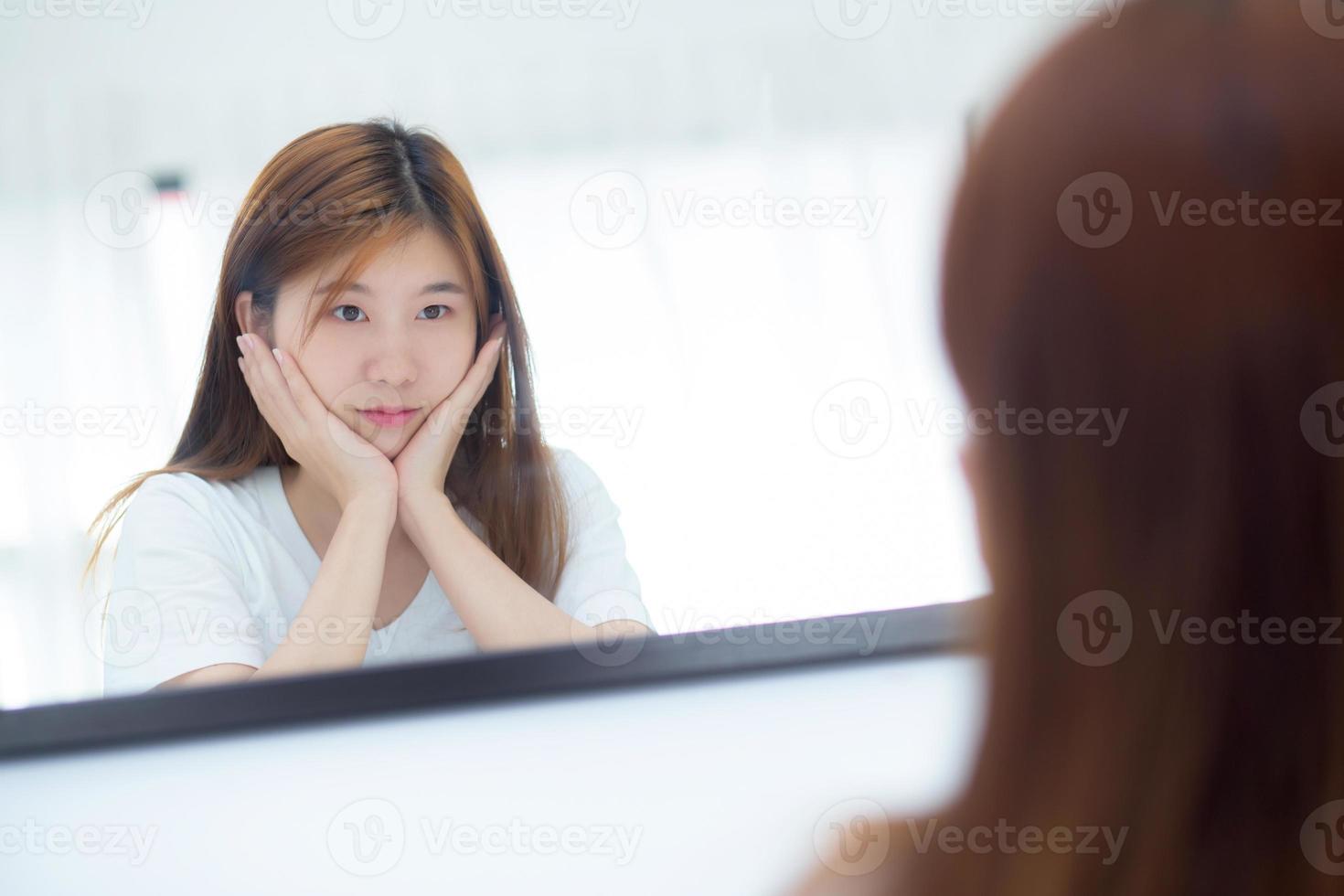 hermosa de retrato mujer joven asiática examinando con cara y sonrisa mirando en el espejo en el dormitorio, chica belleza de maquillaje y vestida con reflexión, estilo de vida y concepto de bienestar. foto