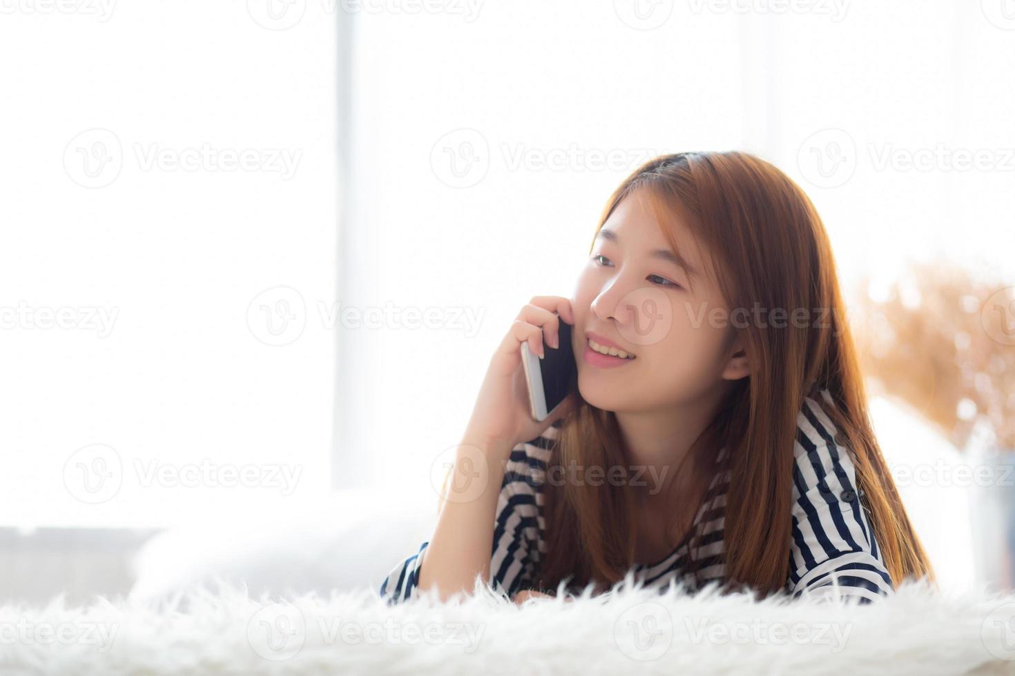 Beautiful young asian woman smiling lying relax on the bed in the morning, girl using mobile smart phone talking enjoy, communication and social network concept. photo