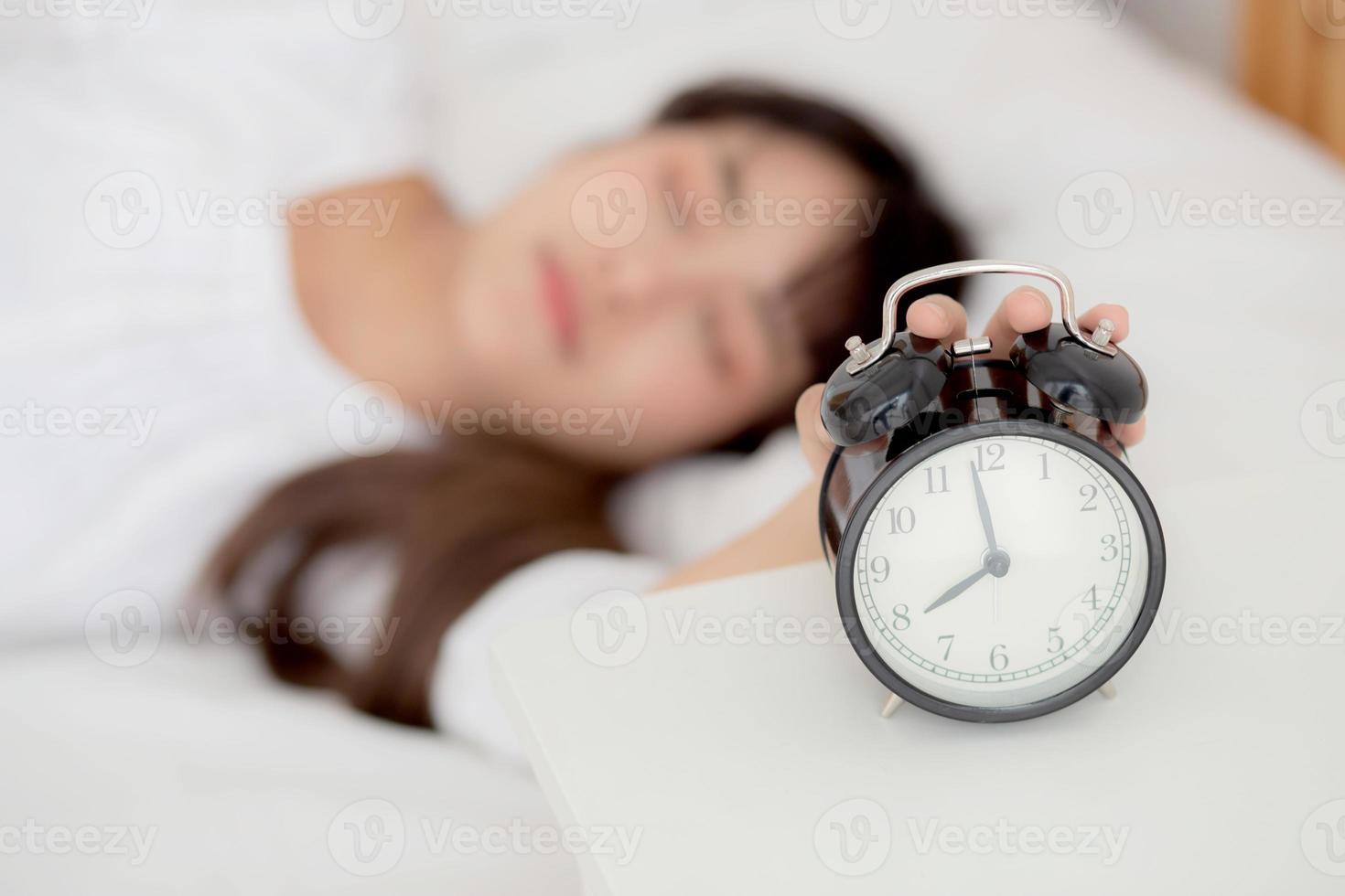 Beautiful asian young woman turn off alarm clock in morning, wake up for sleep with alarm clock, relax and lifestyle concept. photo