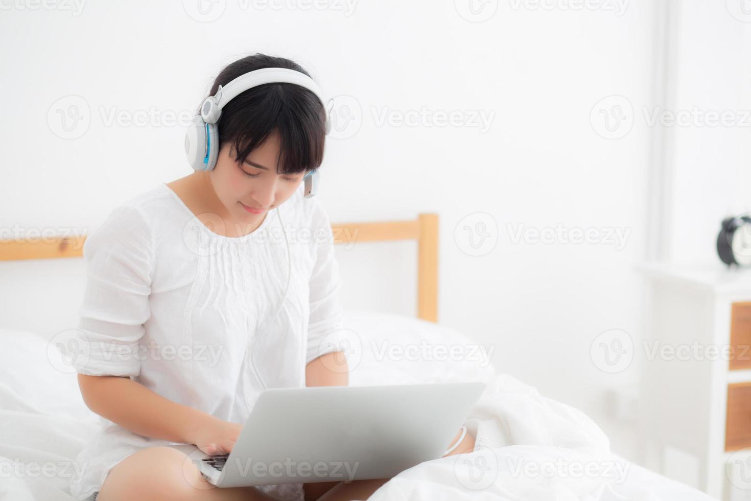 hermosa mujer joven de asia acostada en el dormitorio usando una computadora portátil que muestra chat de videollamada en casa, niña saluda y escucha y habla mensajero, comunicación y concepto de estilo de vida. foto