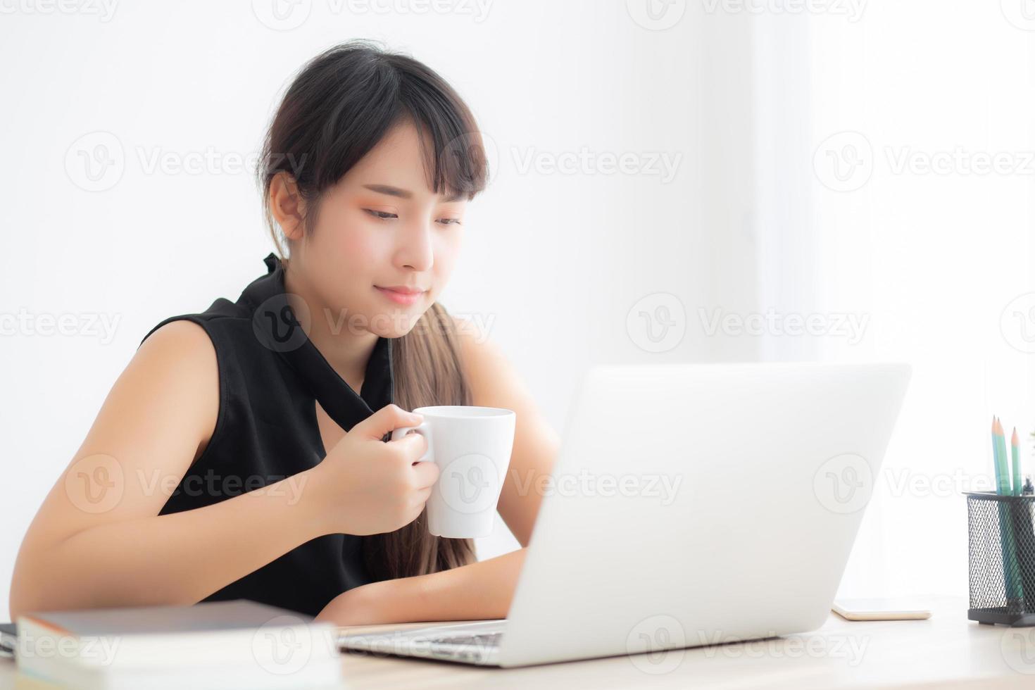 Beautiful young freelance asian woman smiling working and on laptop computer at desk office with professional, girl using notebook and drink coffee, business and lifestyle concept. photo