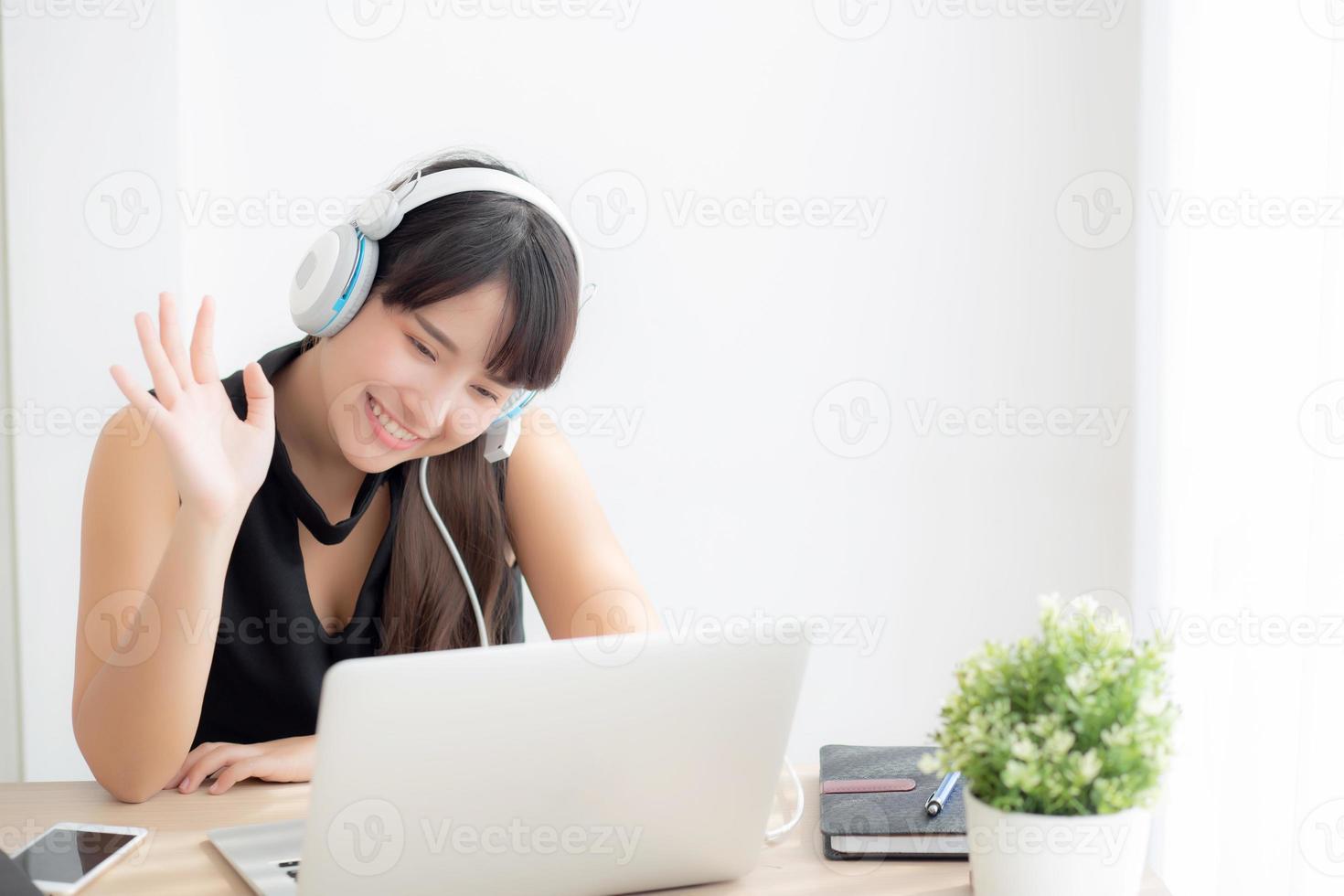 hermosa joven asiática usa auriculares sonriendo saluda usando una videollamada de chat en una computadora portátil, la chica se relaja y disfruta escuchando música en línea, educación, aprendizaje, comunicación y concepto de estilo de vida. foto