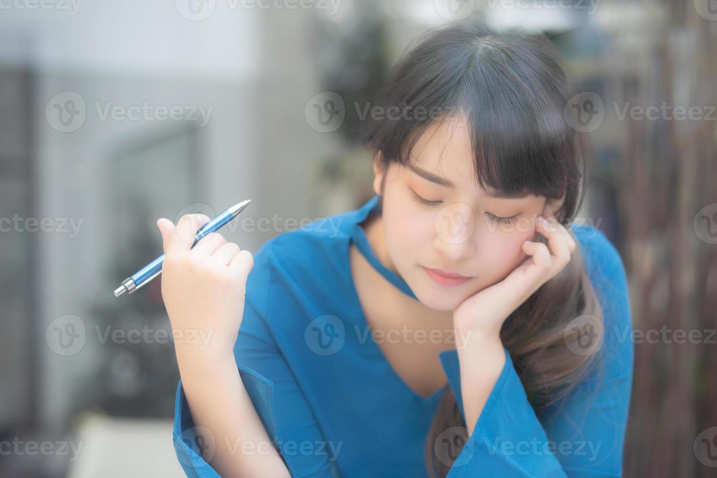 Beautiful young asian woman writer smiling thinking idea and writing on notebook or diary with happy, lifestyle of asian girl is student, female planning working, education and business concept. photo