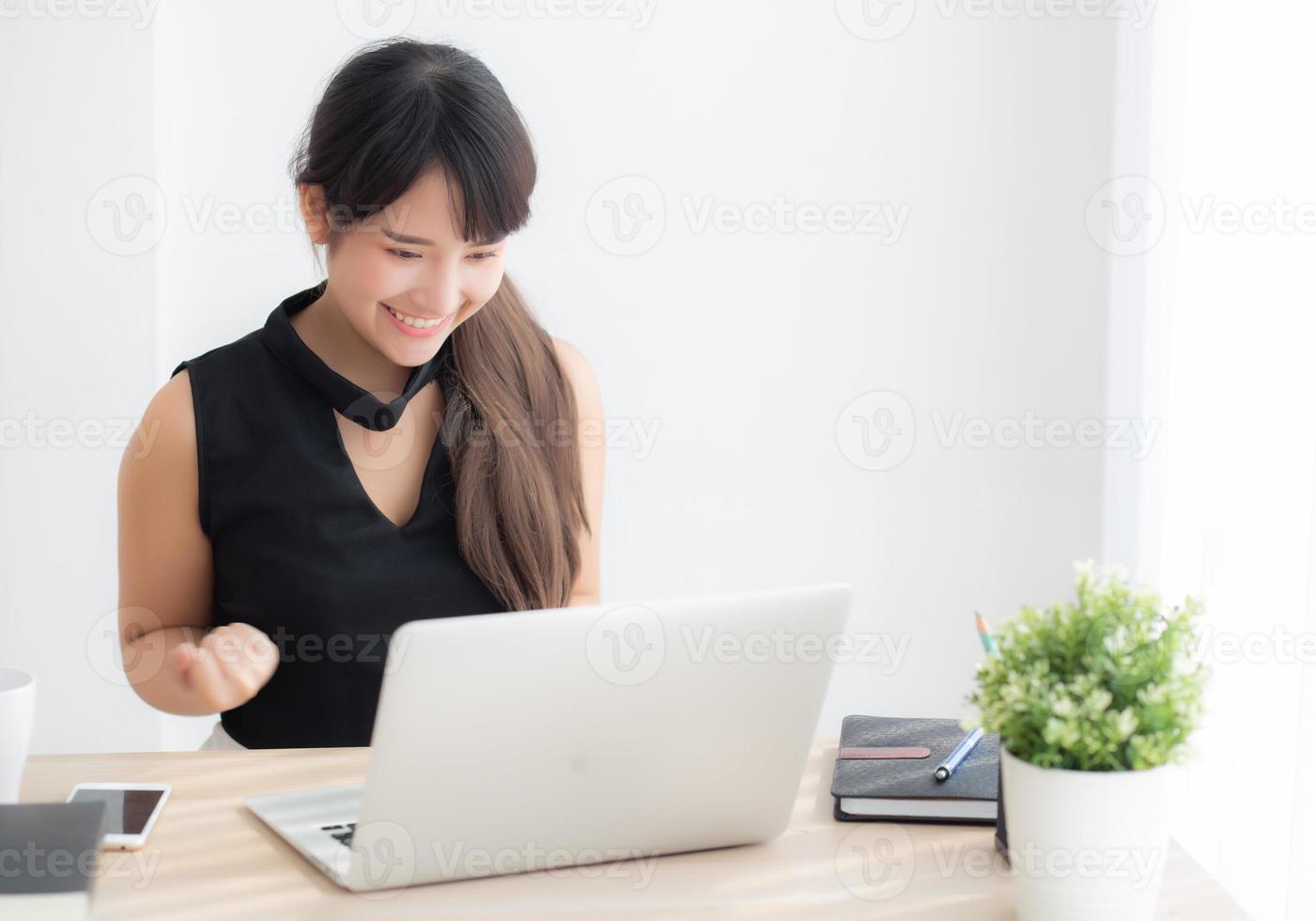 Beautiful portrait asian young woman smile working online laptop computer with happy satisfied sitting on desk office, girl using notebook with excited and glad, business and success concept. photo