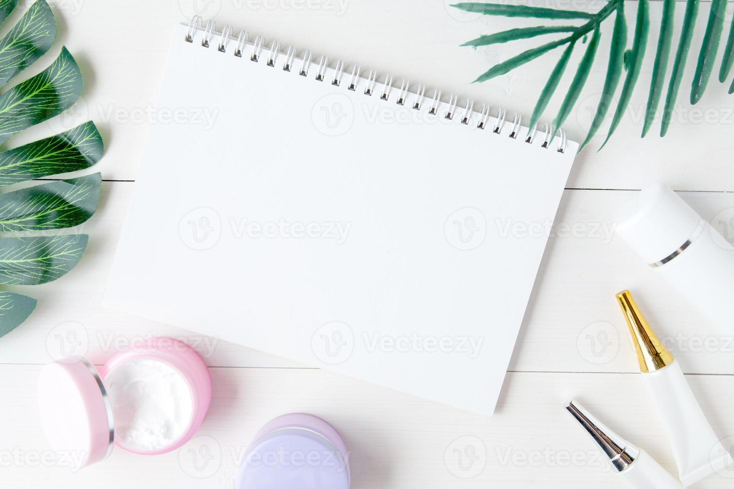 cosmetic and skin care product and notebook and leaves on table, beauty with treatment cream and moisturizing and notepad copy space on wooden desk, health and wellness concept, top view. photo